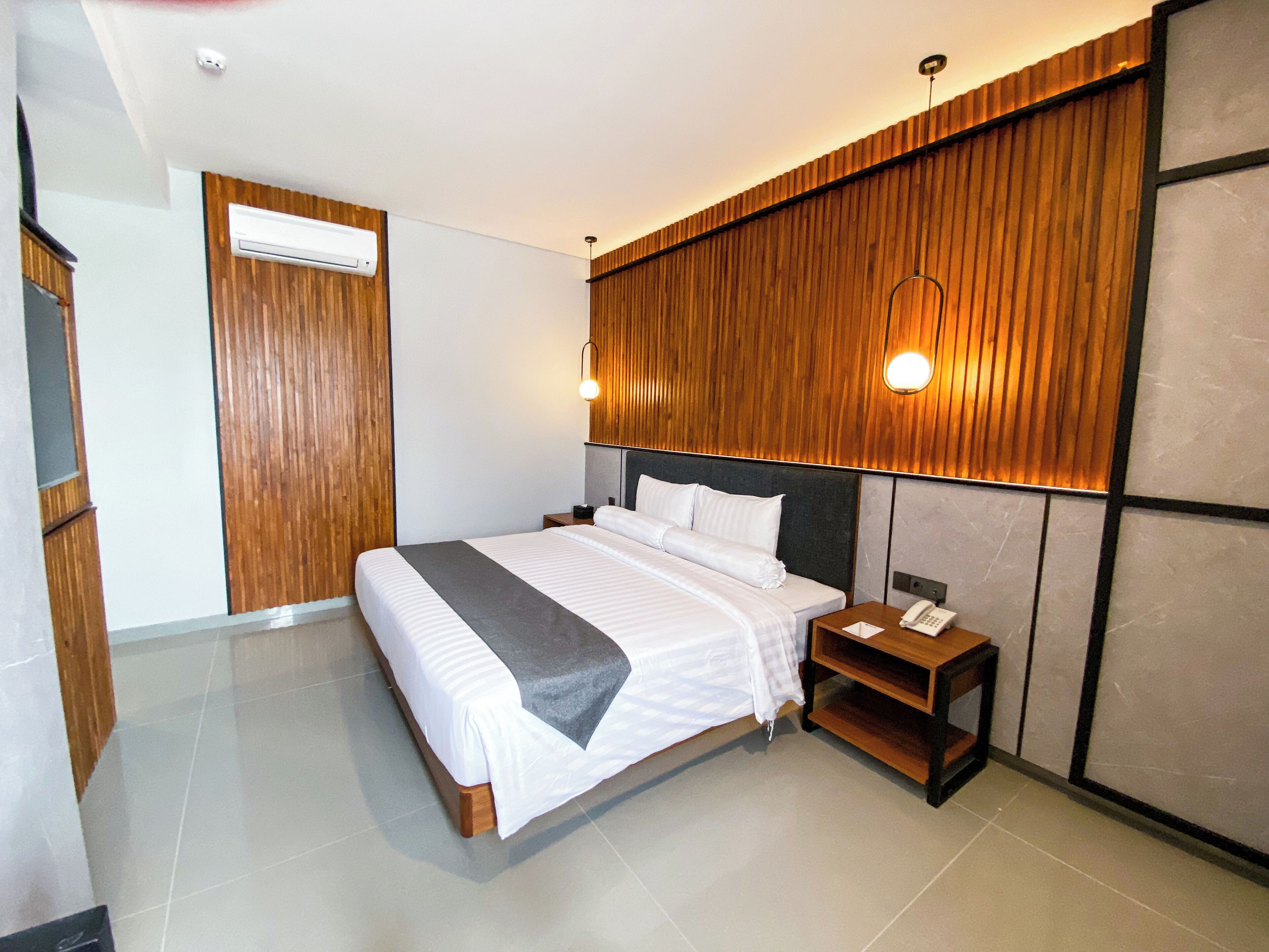 A modern hotel room with a large bed, wooden panel wall, and a bedside table with a phone.