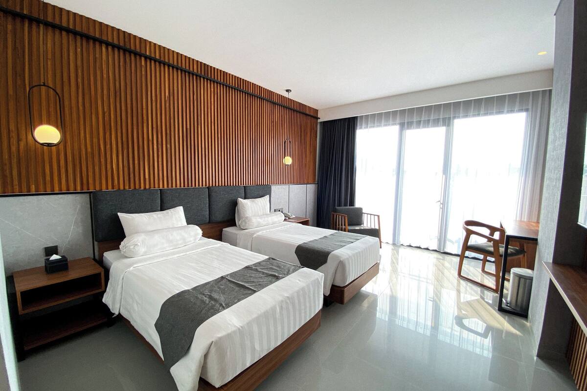 A hotel room with two beds, a desk, a chair, and a large window.