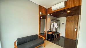 Een moderne hotelkamer met een grijze bank, een houten bijzettafeltje, een spiegel en een houten garderobe.