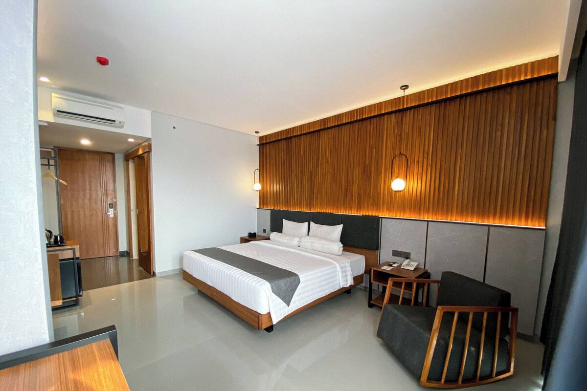 A modern hotel room with a large bed, a desk, a chair, and a wooden accent wall.