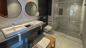 Een moderne badkamer met twee wasbakken, een grote spiegel, een douche en een houten bankje.