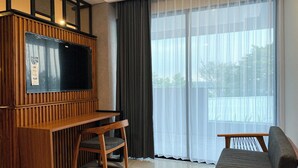 Een moderne woonkamer met een houten entertainmentmeubel, een flatscreen televisie, een bank en een groot raam met transparante gordijnen.