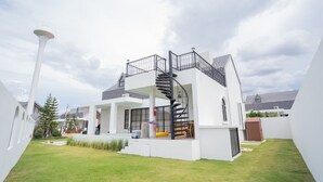 A modern house with a spiral staircase, a covered outdoor area, and a well-maintained lawn. - Oxygen Valley Khao Yai B2 (Pak Chong)