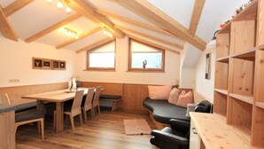 A cozy room with a wooden dining table, chairs, a sofa, and a built-in bookshelf. - Apartment 'Melissa' with Mountain View, Balcony and Wi-Fi (Zellberg)