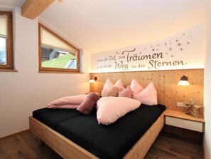 A bedroom with a wooden bed, a wall-mounted light, and a window with a view of a green landscape.