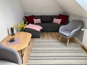 Un espacio habitable estilo loft acogedor con un sofá de color gris oscuro, un sillón gris, una mesa de comedor de madera y una alfombra estampada.