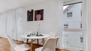 Een moderne eetruimte met een ronde tafel, witte stoelen en een groot raam met uitzicht op een gebouw.