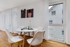 A modern dining area with a round table, white chairs, and a large window with a view of a building.