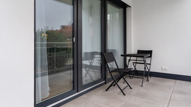 Een balkon met een glazen deur, twee stoelen en een kleine tafel.