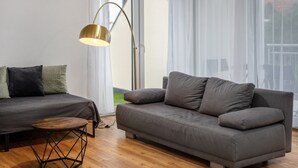 Een moderne woonkamer met een bank, een rond houten bijzettafeltje en een vloerlamp.