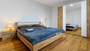 Een moderne slaapkamer met een houten bed, nachtkastje, spiegel en een houten garderobe.