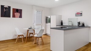 Een moderne keuken met witte kasten, een inbouwoven en een spoelbak. Er is een eethoek met twee witte stoelen en een kleine ronde tafel.