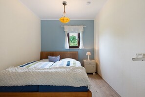A bedroom with a bed, a nightstand, a lamp, a window with curtains, and a hanging light fixture.