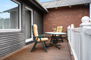 A wooden deck with two chairs and a table, a brick wall, and a white fence.