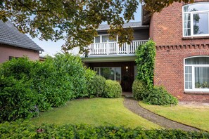A two-story brick house with a white balcony, a brick pathway, and well-maintained greenery.