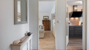 A hallway leading to a living room and kitchen area with a wooden floor, a mirror, and a cabinet. - Apartment 'Hoper Mühle' with Balcony and Wi-Fi (Sankt Michaelisdonn)