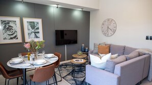 Una sala moderna con un sofá gris, un comedor con una mesa redonda y dos obras de arte florales enmarcadas en la pared.
