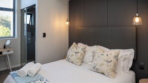 Una cama bien hecha con almohadas estampadas, una mesita de noche con espejo y un pequeño taburete.