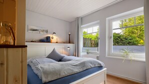 Un dormitorio con cama, lámparas de noche, una ventana con vistas a la vegetación y suelo de madera.