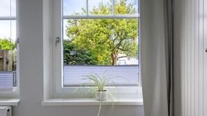 Una ventana con una planta en maceta, una pared blanca y vistas a un árbol y una valla.