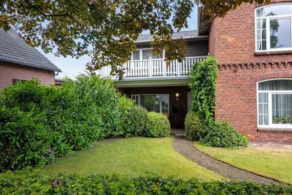 A two-story brick house with a white balcony, a brick pathway, and well-maintained greenery.