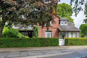 A two-story brick house with a small attached garage, a well-maintained hedge, and a paved driveway.
