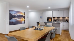 Una cocina moderna con armarios blancos, una mesa de comedor de madera y un cuadro de un lago.
