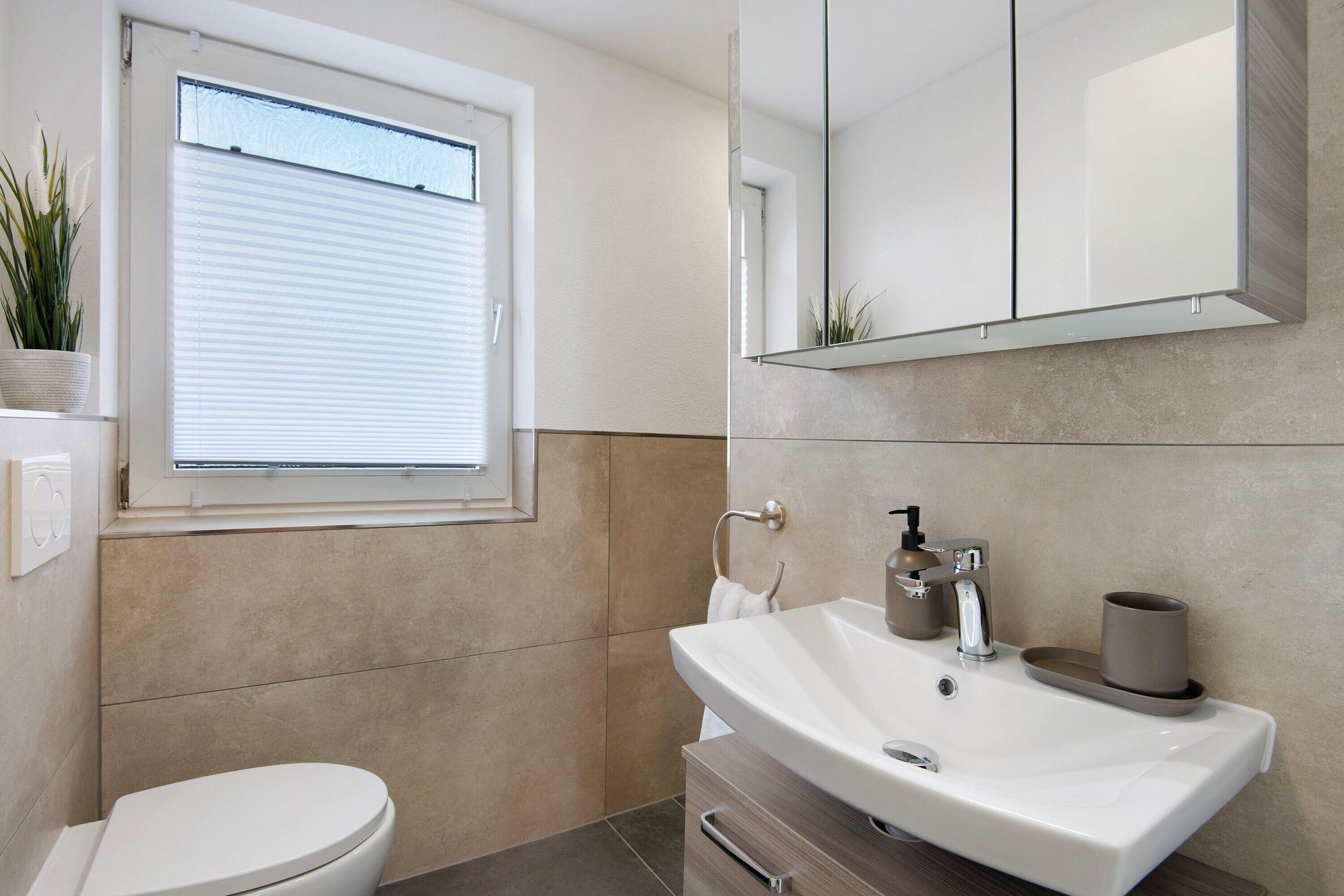 A bathroom with a toilet, a sink, a mirror, and a window with blinds.