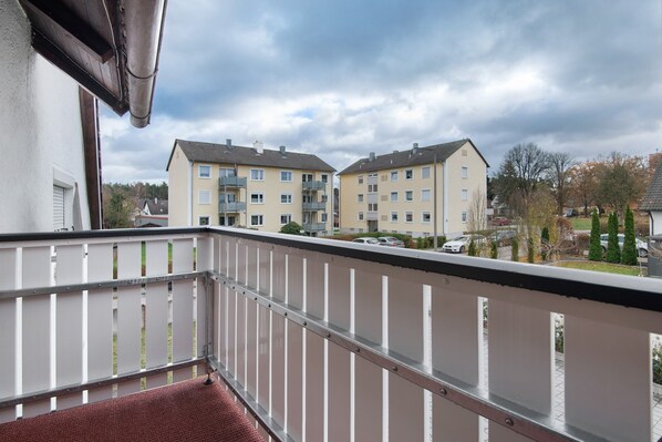 A balcony with a metal railing, overlooking a row of beige apartment buildings with multiple floors and balconies.
