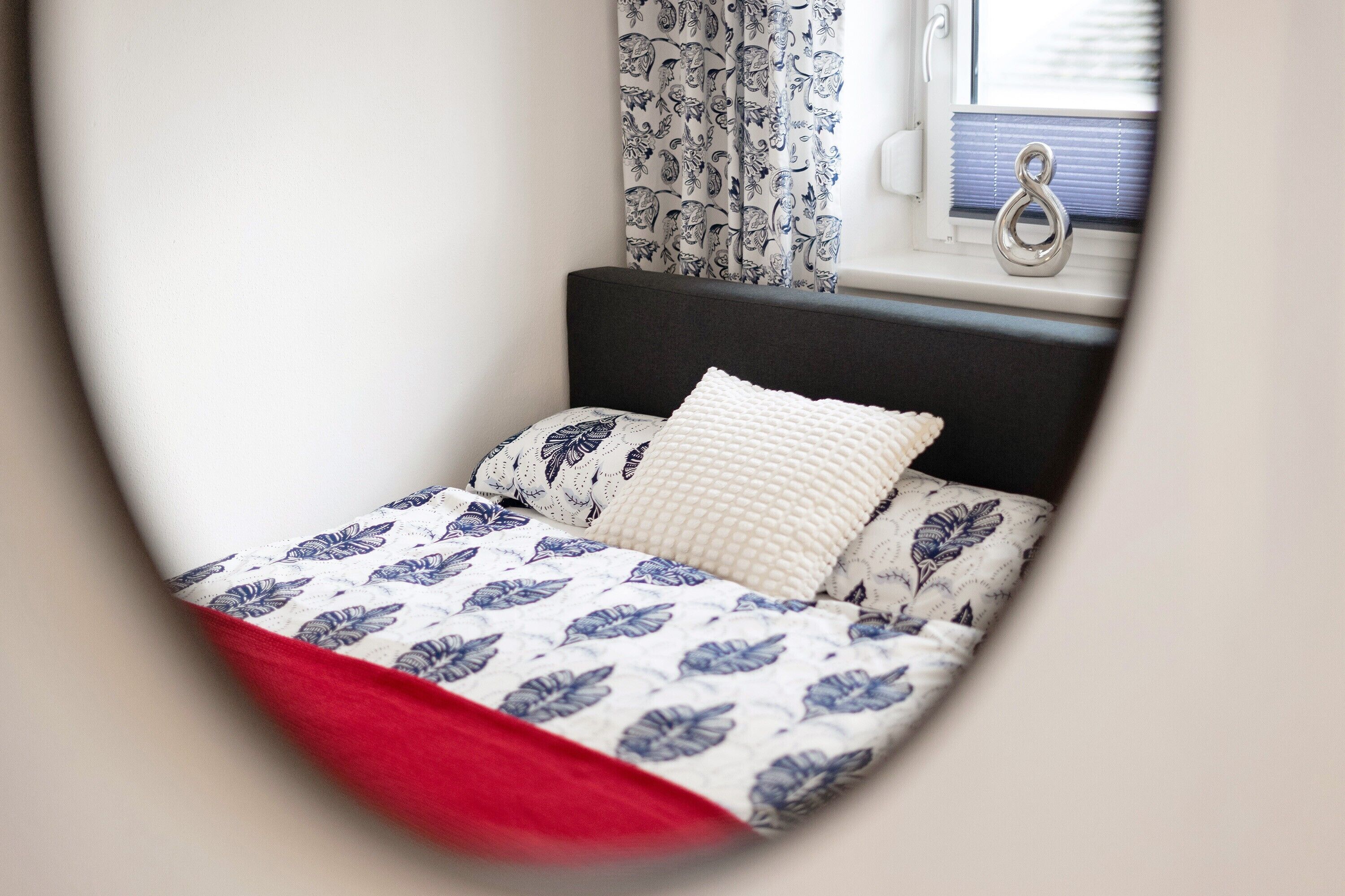 Un lit avec une couvre-lit à motifs floraux, un oreiller blanc et une couverture rouge.