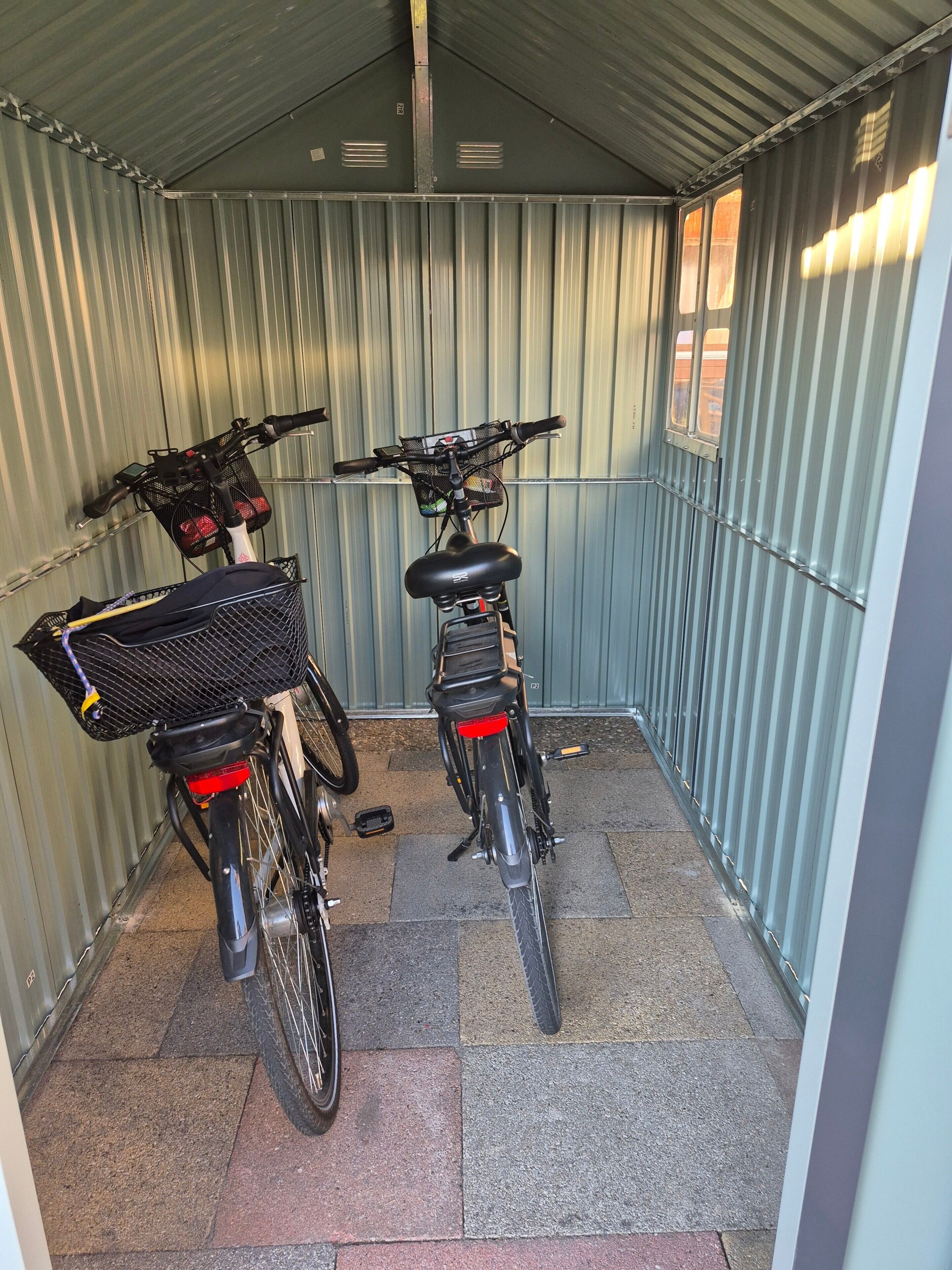 A covered bicycle parking area with two bicycles, each equipped with a basket and a rear light.