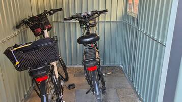 A covered bicycle parking area with two bicycles, each equipped with a basket and a rear light.