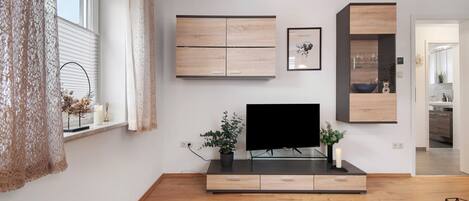 Een moderne woonkamer met een flatscreen televisie, houten kasten en een glazen salontafel.