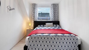Un dormitorio con cama, mesita de noche, ventana con cortinas y un cartel en la pared.