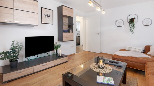 Una sala moderna con una televisión de pantalla plana, una mesa de centro de vidrio, un sofá de cuero marrón y una decoración minimalista.