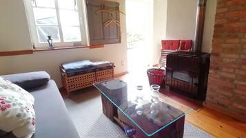 A room with a sofa, a glass-top coffee table, a wooden bench, a fireplace, and a window with curtains.