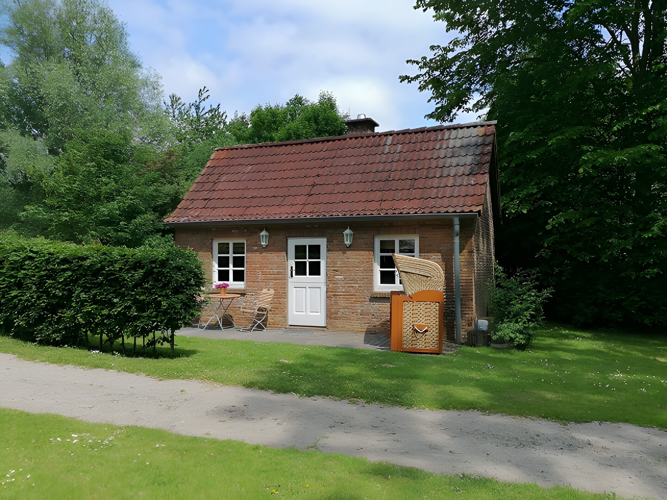 A small brick house with a red-tiled roof, a white door, and a small porch with a chair.