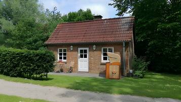 A small brick house with a red-tiled roof, a white door, and a small porch with a chair.