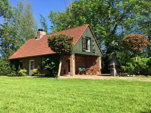 A rustic house with a red-tiled roof, a brick chimney, and a small porch with wooden chairs. - Holiday Home 'Gänsehaus' with Private Terrace and Private Garden (Karolinenkoog)