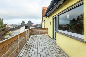 A balcony with a tiled floor, a wooden railing, and a yellow wall with a window.