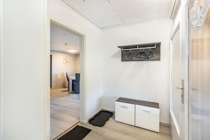 Un couloir avec un porte-manteau, un petit banc et une porte.