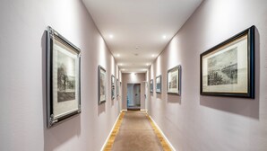 A hallway with framed pictures on the walls, a wooden floor, and a white ceiling.