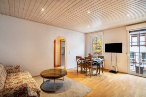 A living room with a sofa, a coffee table, a dining table with chairs, a flat-screen TV, and a large window.