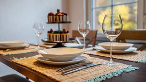 A dining table set with plates, cutlery, and a wine glass, with a cake in the background.