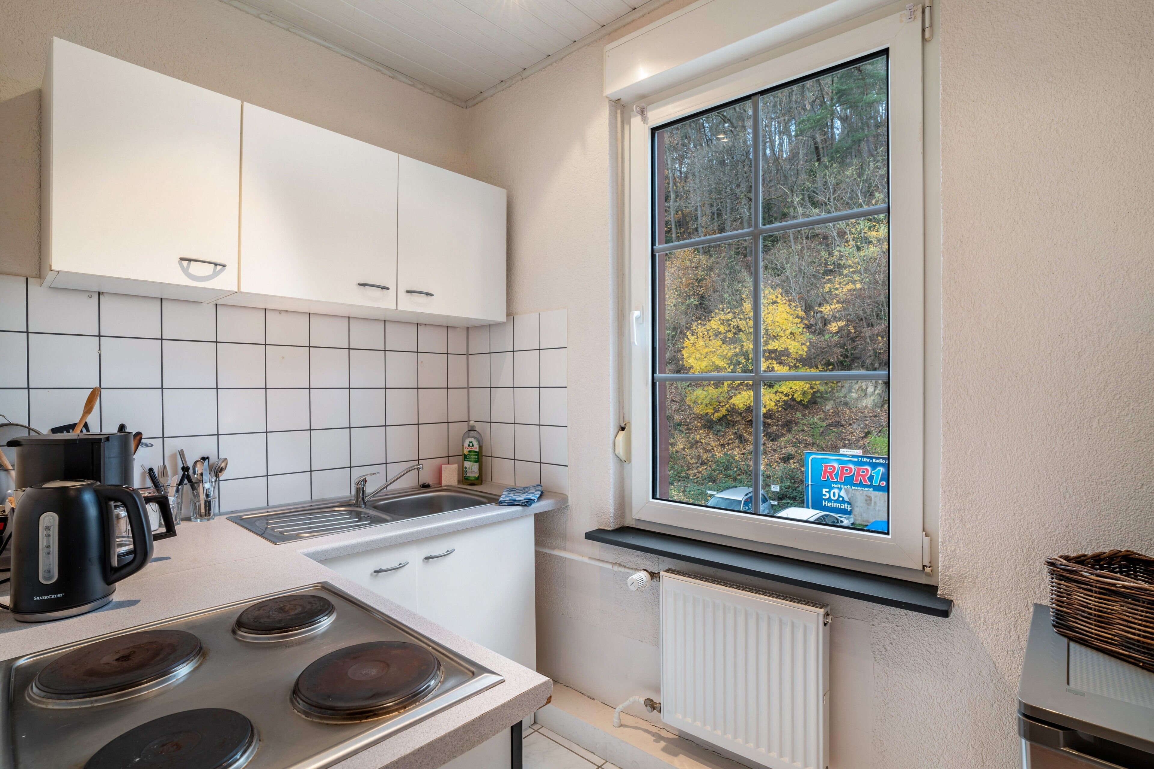 A kitchen with white cabinets, a stove, a sink, and a window with a view of trees.