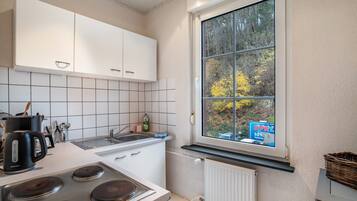 A kitchen with white cabinets, a stove, a sink, and a window with a view of trees.