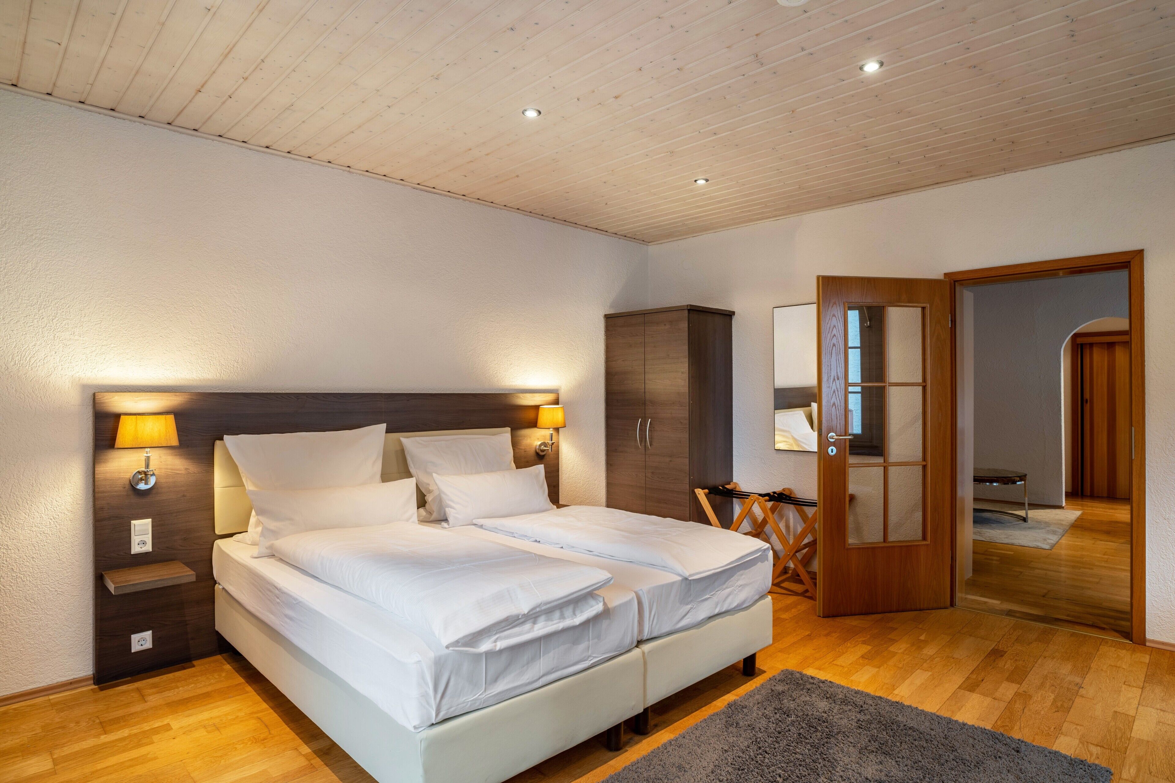 A bedroom with a double bed, bedside lamps, a wardrobe, and a mirror.