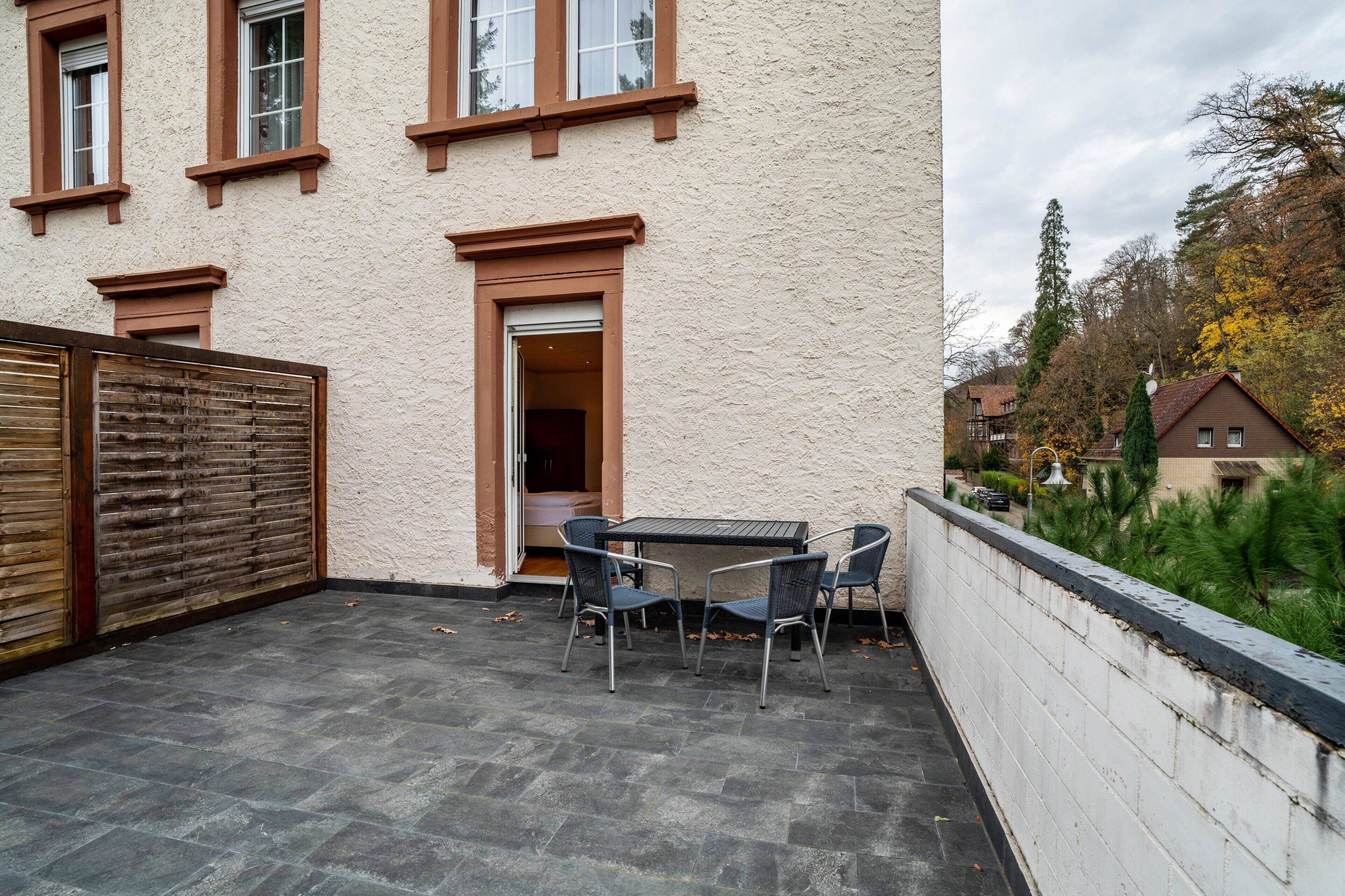 Eine Terrasse mit Tisch und Stühlen, ein Holztor und ein Gebäude mit Fenstern und einer Tür.