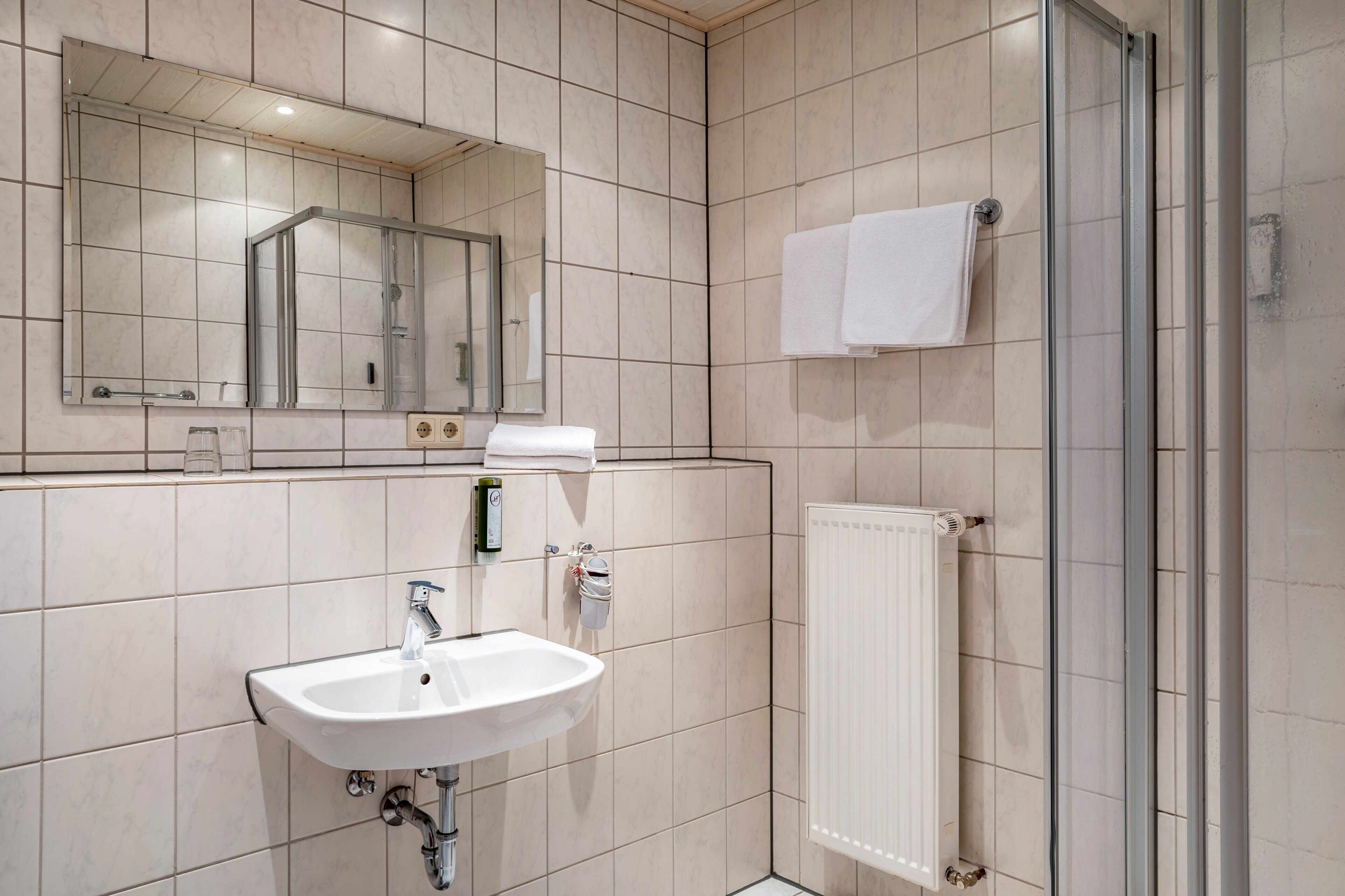 A bathroom with a sink, mirror, towel rack, and shower.