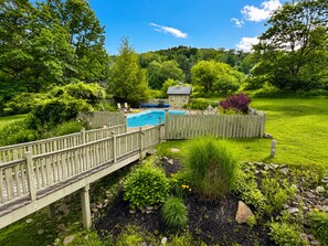 A backyard with a swimming pool, wooden deck, and lush greenery. - The Eagles Nest – Couples Escape - Hot Tub & Views! (Ellicottville)